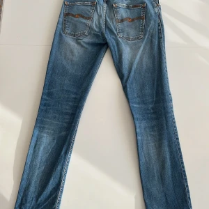 Blå jeans från Nudie Jeans - Snygga blå jeans från Nudie Jeans med klassisk femficksdesign och orange sömmar. Jeansen har en straight passform och är tillverkade i denim med en lätt tvättad look. Perfekta för en avslappnad stil.