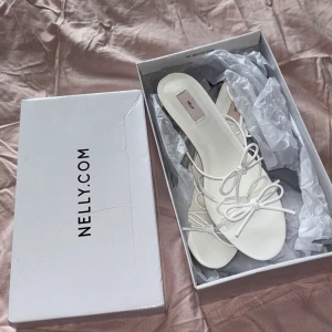 Vita klackskor från Nelly storlek 39 - Eleganta vita klackskor från Nelly med öppen tå och snörning. Perfekta för en stilren look.