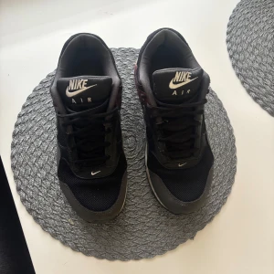 Nike Air sneakers i svart och vinröd - Säljer ett par Nike Air sneakers i svart och vinröd. Skorna har en klassisk design med synlig luftdämpning i sulan och snörning framtill. Perfekta för en sportig look. Finns defekter som syns i bilderna men det går att fixa.