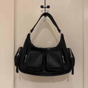 Svart axelväska med flera fickor - Snygg svart axelväska i syntetmaterial från C&A. Väskan har flera praktiska fickor med dragkedjor och en bred axelrem för bekväm användning. Perfekt för att hålla ordning på många småsaker! 