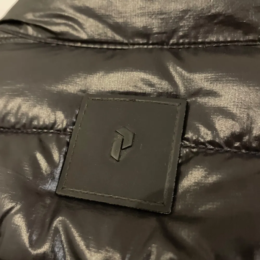Snygg svart dunväst från Peak Performance med dragkedja och två praktiska fickor framtill. Västen har en quiltad design och en diskret logotyp bak. Perfekt för kyligare dagar. Mindre skada finns och framgår i bilderna. . Takit.