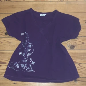 Lila topp med broderade detaljer från Havana - Säljer en lila topp från Havana med v-ringning och korta ärmar. Toppen har vackra broderade blommor och fjärilar i silver på ena sidan. Perfekt för en stilren look.