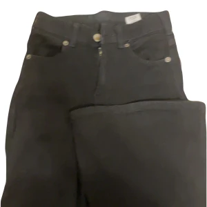 Svarta jeans från Dr. Denim - Snygga svarta jeans från Dr. Denim i modellen Macy. De har en klassisk femficksdesign och en dragkedja med knapp framtill. Perfekta för en stilren look. Jeansen är jätteflared och midjan är ungefär 1-2 cm från naveln. Midjemått:31cm innerbenslängd:75cm materialet är stretchig, knappen har blivit lite brun i mitten men det är inget man märker när man har på dem. 