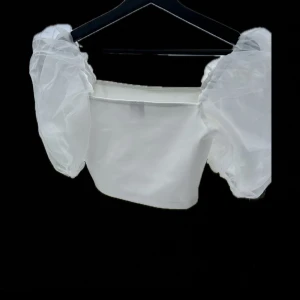 Vit topp från ASOS - Säljer en elegant vit topp från ASOS med puffiga ärmar i ett transparent material. Perfekt för en stilren look. 