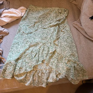 Grön blommig kjol med omlott volang - Charmig grön kjol med blommigt mönster och volangdetaljer. Perfekt för en somrig look med sin luftiga design. 