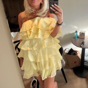 Volang klänning - Säljer en söt gul axelbandslös klänning med flera lager av volanger. Perfekt för sommarens fester och tillfällen. .