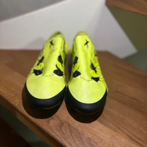 Adidas x15,1 - Säljer ett par iögonfallande gula fotbollsskor med svarta detaljer och snörning. Skorna har en modern design med en mönstrad yta och är perfekta för fotbollsplanen.