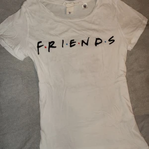 Vit t-shirt med Friends-tryck - Säljer en vit t-shirt från L.O.G.G. med det ikoniska Friends-trycket i svart med färgglada prickar. Perfekt för fans av serien! T-shirten är kortärmad och har en klassisk rund halsringning.