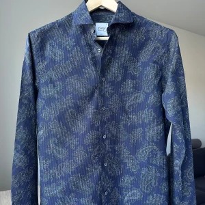 Mönstrad skjorta från Oscar of Sweden - Oscar Jacobson. Indigo färg med snyggt mönster. Slim fit, storlek 40. 100% bomull. Nyskick. Jag säljer många skjortor i samma storlek, kolla gärna på mina övriga annonser för att skapa ett paket. Axelbredd: 47 cm Längd: 77 cm  Casual skjorta, kostymskjorta, smart, mönster, oscar of sweden.
