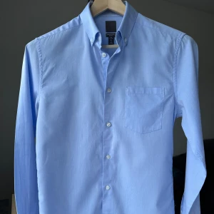 H&M Premium oxfordskjorta ljusblå slim fit, storlek S - Premiumskjorta från H&M, väldigt skön och hög kvalitet. Oxfordskjorta med button down. Slim fit, storlek S. Ljusblå. 100% bomull. Jag säljer många skjortor i samma storlek, kolla gärna på mina övriga annonser för att skapa ett paket. Axelbredd: 43 cm Längd: 72 cm  Kostymskjorta, business, finskjorta, oxford.