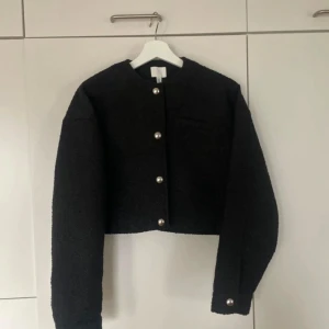 Svart kavaj med pärlknappar - Snygg svart kavaj med unika pärlknappar framtill. Den har en croppad design och en enkel bröstficka. Perfekt för att ge en elegant touch till din outfit.