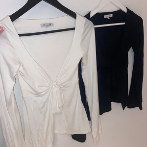 Vit långärmad topp med knyt från Designbysi - Säljer två långärmad toppar från designbysi. Toppen har en v-ringad design med knyt framtill som ger en snygg detalj. Perfekt för att matcha med olika outfits. Båda för 250kr skriv om ni vill köpa separat💕
