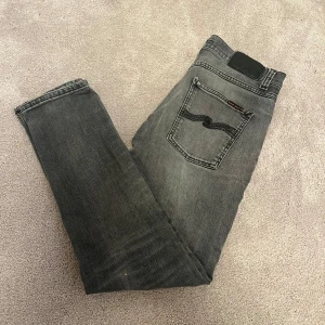 Gråa Nudie Jeans  - Snygga gråa jeans från Nudie Jeans. Jeansen är använda men i bra skick. Jeansen har en cirka 2cm reva/öppning vid högra knät. 