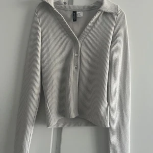 Grå ribbad kofta från Collusion - Säljer en stilren grå ribbad kofta från Collusion. Den har långa ärmar och knappar framtill, perfekt för lager på lager-stil. Passar både till vardags och mer uppklädda tillfällen. Ett måste i garderoben! 🖤
