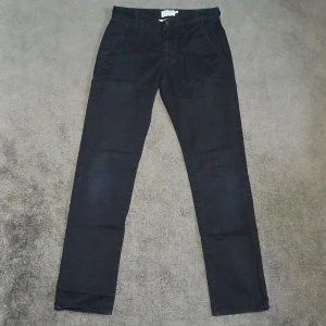 Svarta byxor från Farah - Snygga svarta byxor från Farah i en organisk blandning. De har en klassisk design med knappar och dragkedja framtill. Perfekta för en stilren look.