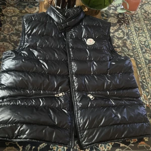 Moncler gui  - Snygg svart dunväst från Moncler med glansig  yta och dragkedja framtill.                                             Äkta⚠️. Qr fungerar utmärkt                                                                Inga byten⚠️.                                                                         Priset kan diskuteras⚠️.                                                           Skick 9/10