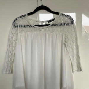 Vit topp med spets - Fin vit blus/topp med spetsdetaljer på axlar och ärmar. Blusen har trekvartsärmar och en luftig passform💗