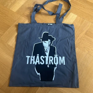 Grå shoppingväska med Thåström-tryck - Säljer en grå shoppingväska från Westford Mill med ett coolt Thåström-tryck på framsidan. Väskan har långa handtag och är perfekt för att bära med sig det nödvändigaste. Tillverkad av etiskt producerat material.