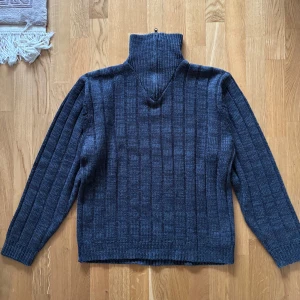 Grå stickad tröja med dragkedja - Säljer en stilren grå stickad tröja med dragkedja i kragen. Tröjan har ett ribbat mönster och långa ärmar, perfekt för kyligare dagar. Den är i storlek XL och passar bra för en avslappnad look. Perfekt för höst och vinter!