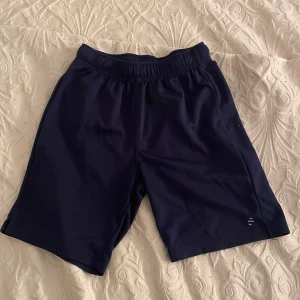 Mörkblå sportshorts från H&M - Säljer ett par mörkblå sportshorts från H&M. De har en elastisk midja för extra komfort och är perfekta för träning. Shortsen är tillverkade i ett lätt och smidigt material som andas bra.