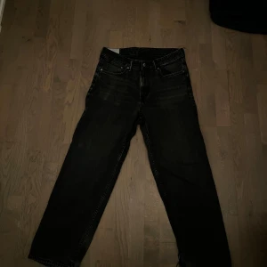 Svarta jeansbyxor från H&M - Säljer ett par svarta loose fit jeans från H&M. De har en avslappnad passform och är perfekta för en casual look. Byxorna har klassisk femficksdesign och är tillverkade i ett slitstarkt material. Skavanker finns.
