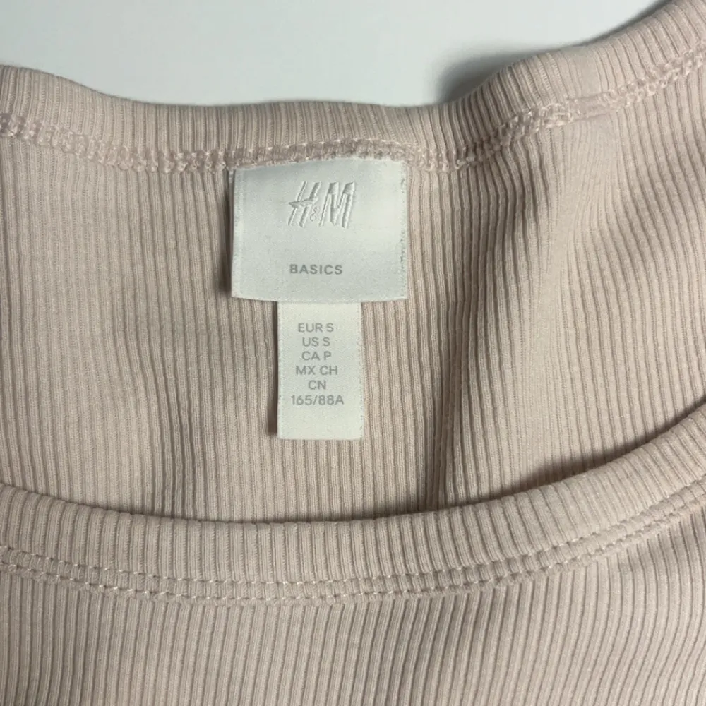 Säljer en stilren beige ribbad topp från H&M Basics. Toppen har en v-ringad design och korta ärmar, perfekt för en enkel och snygg look. Passar bra till jeans eller kjol för en avslappnad stil.. Yläosat.