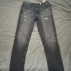 Svarta jeans från Jack & Jones - Snygga svarta jeans från Jack & Jones med slitna detaljer för en cool look. De har en klassisk femficksdesign och en bekväm passform. Perfekta för en avslappnad stil.