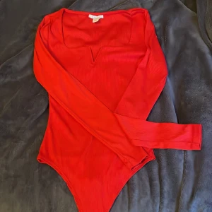 Röd ribbad bodysuit  - Snygg röd ribbad bodysuit med långärmad design. Perfekt för att skapa en stilren look. Tillverkad i Turkiet och passar utmärkt för både vardag och fest.