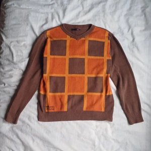 Brun och orange rutig tröja - Säljer en brun tröja med ett orange rutmönster på framsidan.  Perfekt för en unik och färgglad stil. Uppskattad storlek XS-S