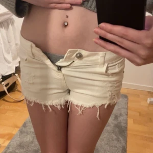 Vita jeansshorts - Snygga vita lågmidjade  jeansshorts med slitna detaljer och fransig kant. De har en knapp och dragkedja framtill samt fickor både fram och bak. Den är två nitar och en fin detalj på backfickan. Perfekta för en avslappnad sommarlook!
