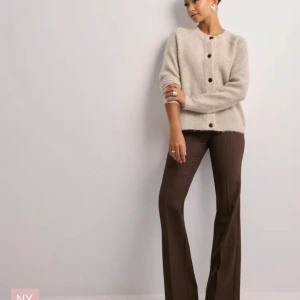 Beige stickad kofta från Nelly - Snygg beige stickad kofta från Nelly med svarta knappar. Perfekt för en stilren och mysig look. Koftan har långa ärmar och en rund halsringning.