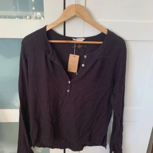 Mörklila långärmad topp från Holebrook - Säljer en stilren brun långärmad topp från Holebrook. Toppen har en knappdetalj framtill och en liten broderad logga på baksidan. Perfekt för en avslappnad och bekväm stil. Helt ny med lapp kvar. Hör av dig vid intresse! 💜
