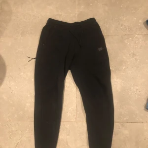 Nike tech byxor - Säljer ett par svarta mjukisbyxor från Nike. Byxorna har en bekväm passform med snörning i midjan och är perfekta för en avslappnad stil. De är tillverkade i mjukt material och har en liten Nike-logga på benet.