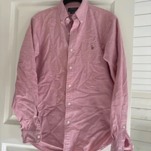 Rosa skjorta från Polo Ralph Lauren - Snygg rosa skjorta från Polo Ralph Lauren i slim fit. Skjortan har långa ärmar och klassiska knappar framtill. Perfekt för en stilren look med den ikoniska loggan broderad på bröstet. Väldigt fint Sick typ aldrig använd. 