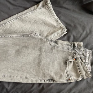 Grå jeans  - Snygga grå jeans med en vid passform och midwaist design. Perfekta för en avslappnad stil. De har en klassisk femficksdesign och stängs med dragkedja och knapp.