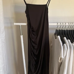 Mörk brun klänning - Mid klänning med veckade detaljer framtill samt en slits.