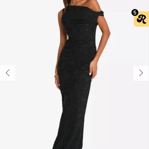 Svart axelbandslös långklänning - Elegant svart långklänning med axelbandslös design och figurnära passform. Klänningen har ett subtilt mönster och är perfekt för en stilfull kväll. Den smickrande silhuetten ger en sofistikerad look.