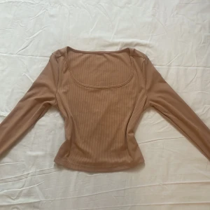 Beige ribbad topp - Säljer en stilren beige ribbad topp med långa ärmar. Toppen har en rundad halsringning och är perfekt för en enkel och snygg outfit. Toppen är midjekort och tajt mot kroppen plus helt oanvänd och bara provad.