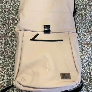 Beige ryggsäck från Be.Bag - Snygg beige ryggsäck till salu. Den har en praktisk dragkedja framtill och justerbara axelband för maximal komfort. Perfekt för dagligt bruk och resor. Den innehåller flera fickor.