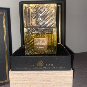 Khamrah Eau de Parfum från Lattafa - Elegant parfymflaska med ett unikt mönster i glaset. Khamrah från Lattafa är en Eau de Parfum på 100 ml. Flaskan har en fyrkantig form med en gyllene vätska inuti och ett matchande lock. Perfekt för den som söker en lyxig doftupplevelse.(Skriv för lägre pris)