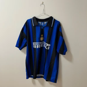 Retro Inter Milan fotbollströja - Säljer en klassisk blå och svart randig fotbollströja från Nike med Pirelli-logga på framsidan. Tröjan har korta ärmar och en krage. Perfekt för fotbollsfans!