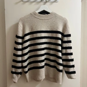 Randig tröja från H&M - Säljer en mysig randig tröja från H&M i beige och svart. Tröjan har långa ärmar och en ribbad krage samt nederkant. Perfekt för en avslappnad stil.
