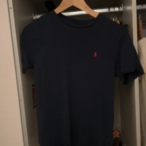 Mörkblå t-shirt från Ralph Lauren - Snygg mörkblå t-shirt från Ralph Lauren med det klassiska röda logotypen på bröstet. Perfekt för en stilren och avslappnad look.använd men inga tecken på det, inga hål eller defekter. köpt för 595 säljer för 250