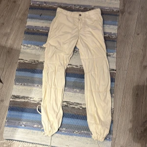 Beige cargopants från Killah - Säljer ett par beige cargopants från Killah med flera praktiska fickor och snörning vid bensluten. Byxorna har en knapp och dragkedja framtill för enkel stängning. Perfekta för en avslappnad stil. Byxa från -90talet. Fint skick! 