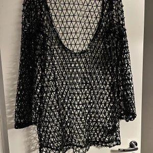 Svart glittrig klänning från NA-KD - Oanvänd snygg svart glittrig klänning från NA-KD med öppen rygg och ett nätliknande mönster. Perfekt för en kväll ute med sina glittrande detaljer. Klänningen har långa ärmar och en unik design som verkligen sticker ut.