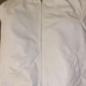 Vit bomberjacka från Moncler - Säljer en stilren vit bomberjacka från Moncler. Jackan har en dragkedja framtill och ribbade muddar vid ärmslut och nederkant. Perfekt för en minimalistisk look. Står moncler över hela jackan men i vitt så det syns på nära håll. Passar S.