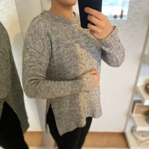 Grå stickad tröja - Mysig grå stickad tröja med lång ärm och ribbade detaljer vid ärmslut och nederkant. Perfekt för kyliga dagar.