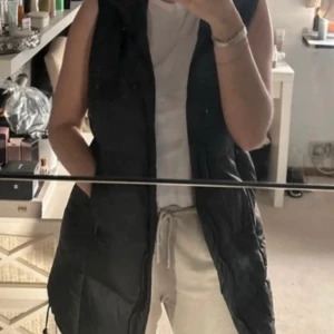 Svart dunväst från Zara - Snygg svart dunväst från Zara med huva och dragkedja. Perfekt för kyliga dagar och enkel att matcha med olika outfits. Västen har en quiltad design som ger extra värme och stil.