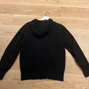 Svart kashmir hoodie från Soft Goat - Säljer en lyxig svart hoodie från Soft Goat i 100% kashmir. Den har en dragkedja framtill och en bekväm huva. Perfekt för att hålla sig varm och stilren under kyliga dagar. Passar som bäst om man är 170-180. Det finns hål på armbågarna som man kan fixa därav priset 