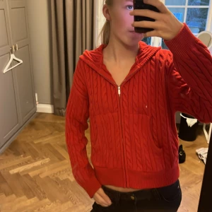 Röd stickad hoodie från Zara - Säljer en snygg röd stickad hoodie från Zara med dragkedja och kabelstickat mönster. Tröjan har långa ärmar och en mysig huva, perfekt för kyliga dagar. Passar både till jeans och kjol. 🧶